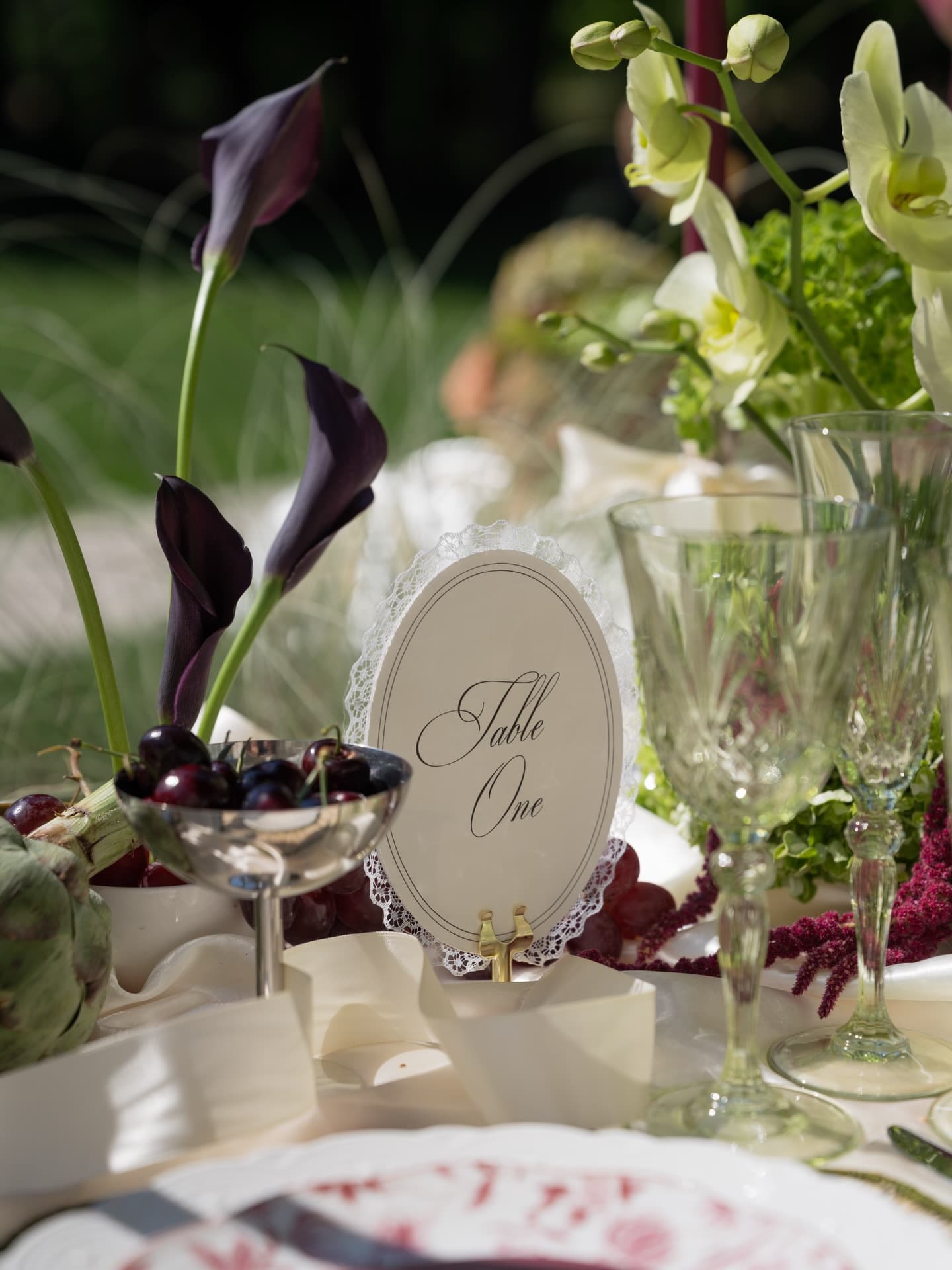 A Table One place card beside black calla lilies, crystal glassware and a silver compote of grapes